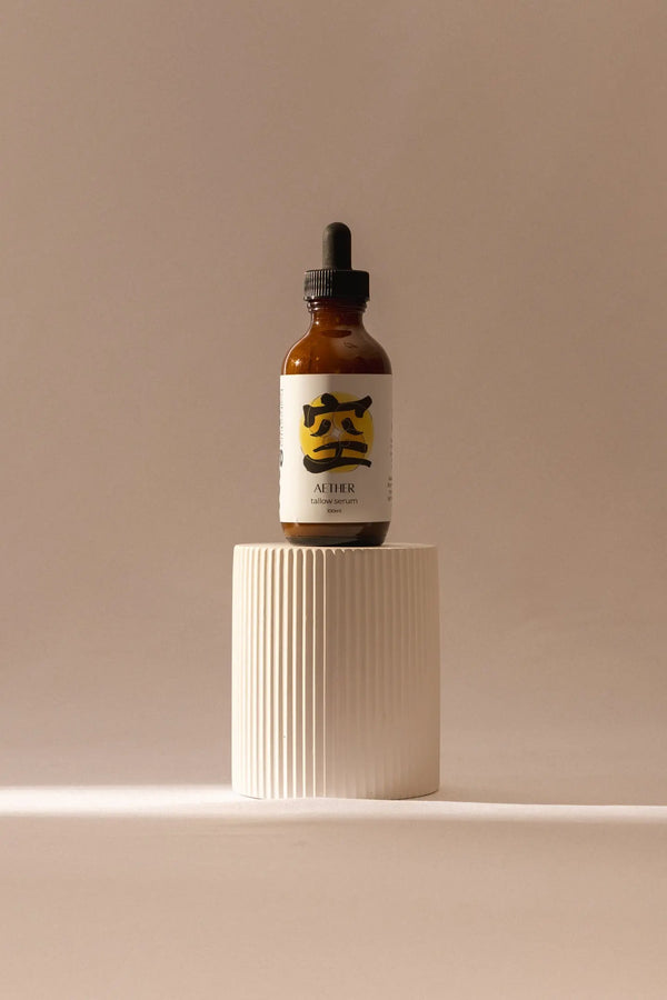 Bottle of aether tallow serum with dropper on a white pedestal against a beige background