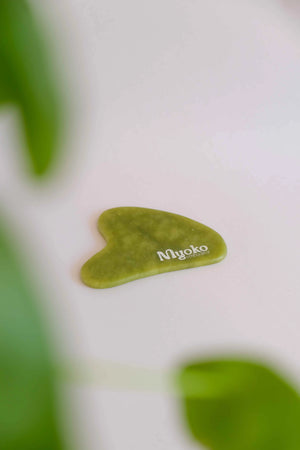 Green heart-shaped gua sha tool with 'Myoko' branding on a white background