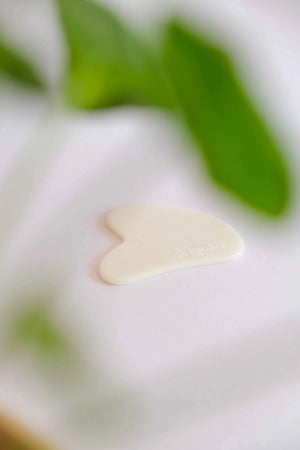 Heart-shaped white gua shaon a white surface with green leaves in the background
