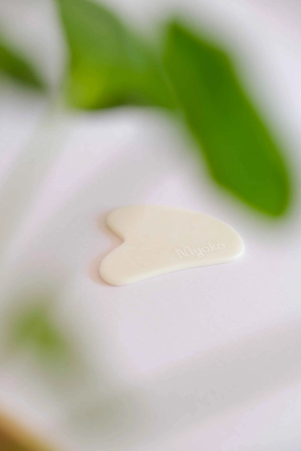 Heart-shaped white gua shaon a white surface with green leaves in the background