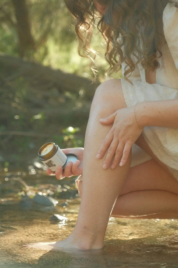Person sitting by a stream applying Tallow cream to their leg.