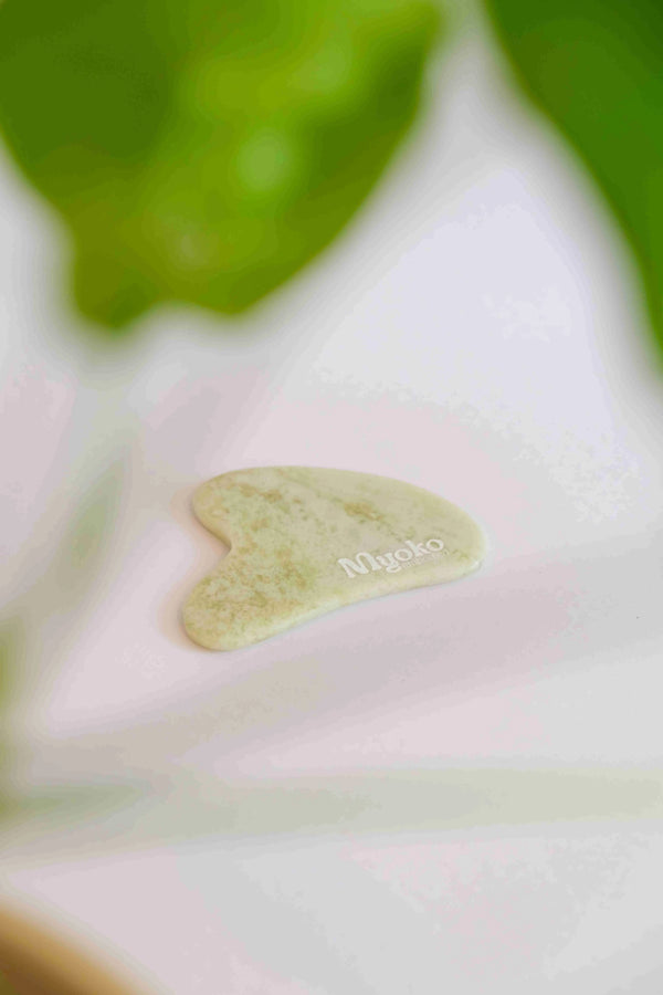 jade stone gua sha tool with 'Myoko' branding on a blurred natural background